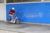 A rider on a small motorbike passing a bright blue wall